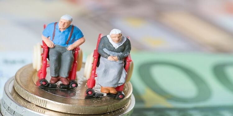 Poppetje van oudere man en vrouw in rolstoel op een stapeltje muntgeld met daaronder biljetten
