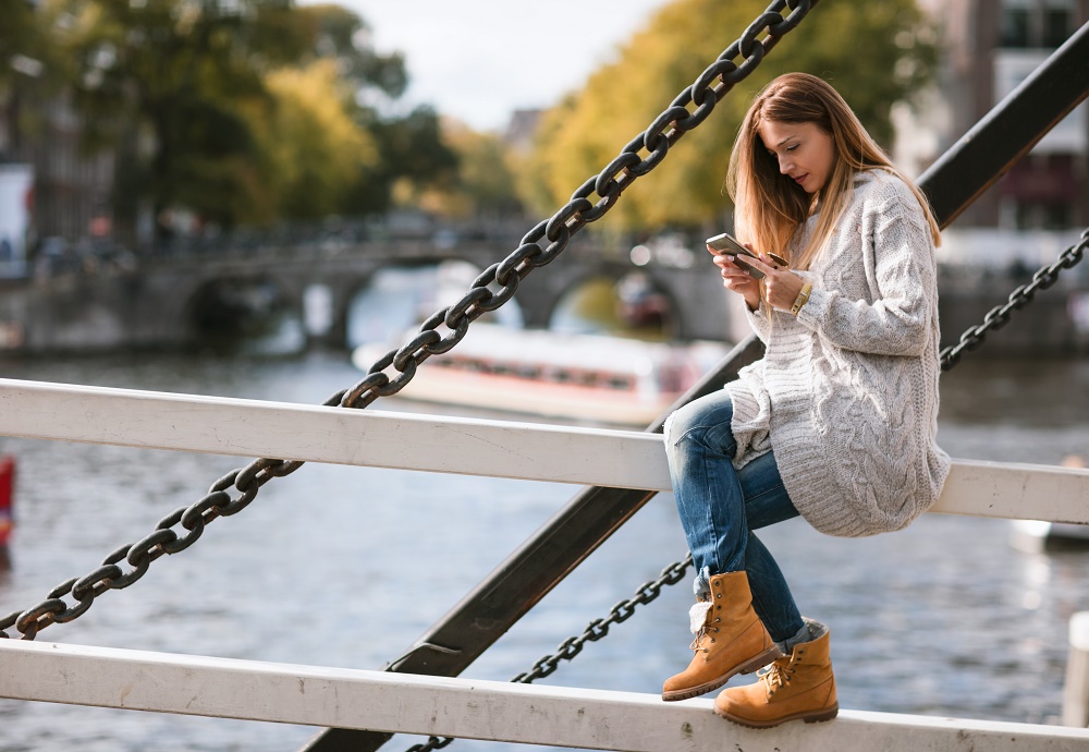 Vrouw met telefoon die zit op de reling van een brug