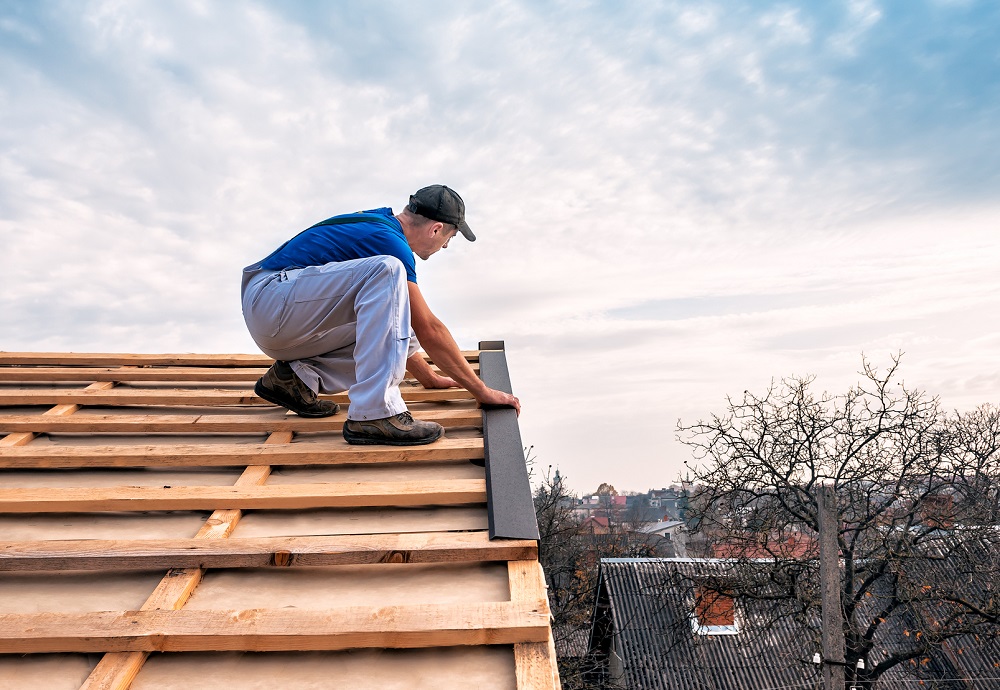 Man met pet staat op dak en installeert een dakrand